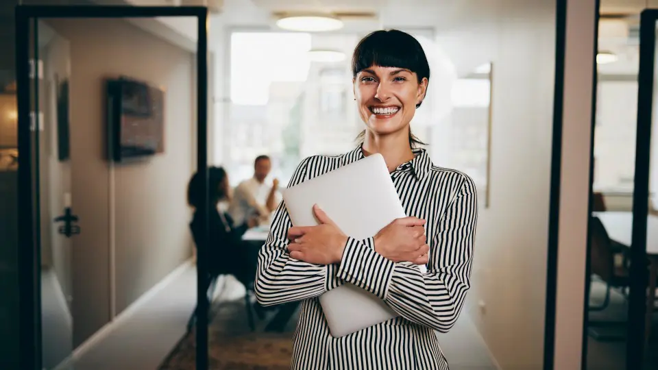 Lächelnde Frau mit Laptop vor Büro