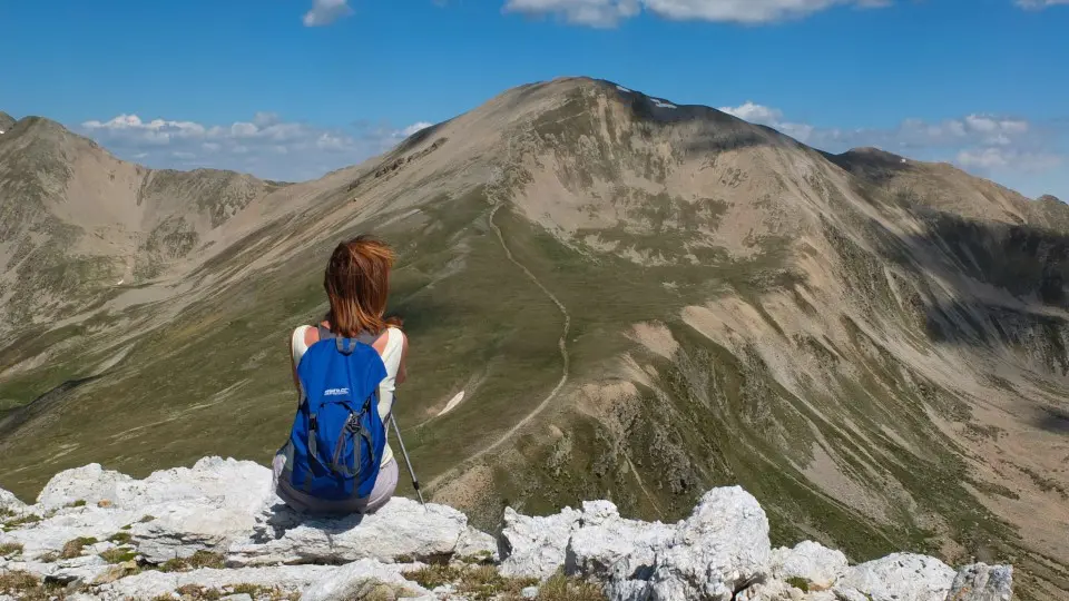 Frau sitzt auf Berg und blickt auf einen langen Weg
